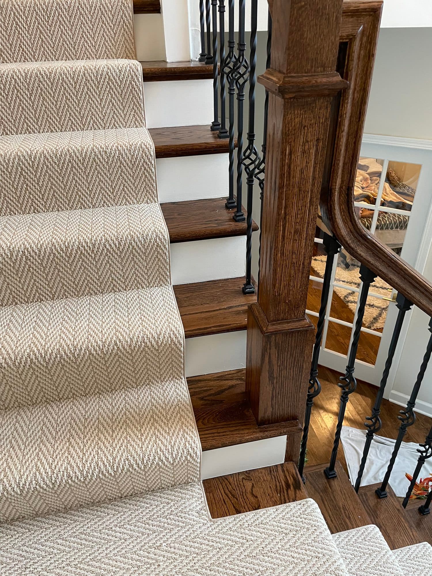 Close side view of the bound herringbone runner on oak stair treads next to the newel post and curved handrail