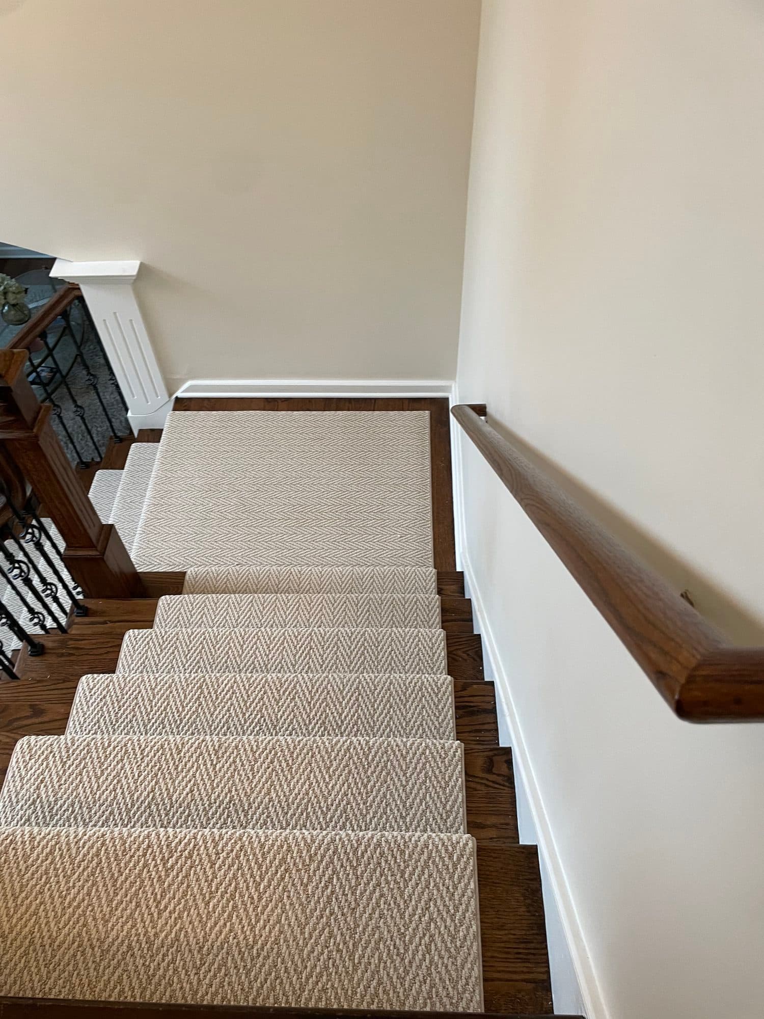 View down the stairs from the top showing the herringbone runner on oak treads with a wall handrail on the right